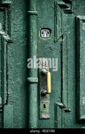 Vecchio scolpita in legno porta dipinta con olio verde vernice con impugnatura in bronzo e acciaio serratura, street elemento di design della tipica e antica città europea. Foto Stock