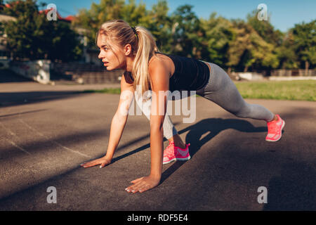 Giovane donna runner scendere per un tempestivo avvio su campo sportivo in estate. Attiva uno stile di vita sano Foto Stock