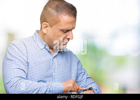 Età media arab business man over isolato background controllando il tempo su orologio da polso, rilassato e fiducioso Foto Stock