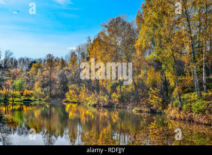 Golden fogliame di autunno alberi intorno al lago riflette in acqua del lago - autunno pittoresco paesaggio a caldo e soleggiato settembre meteo con blu chiaro Foto Stock