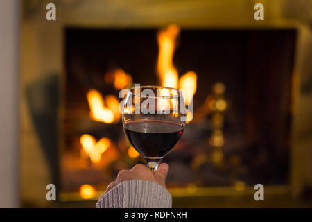 Close up uomo holding e di bere il vino rosso il vetro da fuoco di legno aperto posto rilassante e piacevole momento di quiete a casa in vacanza invernale vacanza, Chr Foto Stock