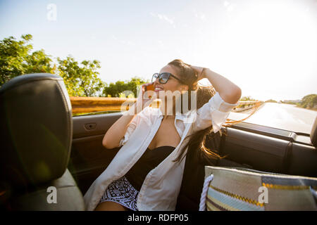 Giovane donna utilizza il telefono cellulare e la seduta in cabriolet al giorno di estate Foto Stock