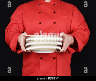 Cuocere in rosso uniforme tiene nelle sue mani una pila di bianco rotondo per le placche vuote Foto Stock