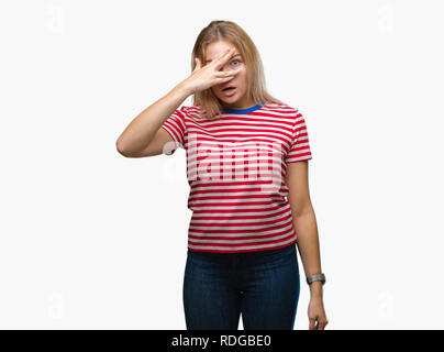 Giovane donna caucasica su sfondo isolato peeking in stato di shock che copre il viso e gli occhi con la mano, guardando attraverso le dita con imbarazzo espressione. Foto Stock