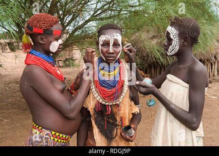 Tre giovani donne Karo mettendo sul make-up, pitture facciali, Omo river valley, l'Etiopia meridionale, Africa Foto Stock
