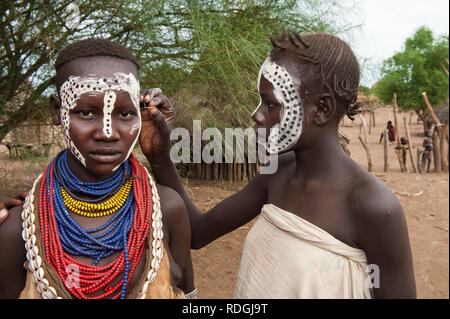 Giovane donna Karo getting make-up, pitture facciali, Omo river valley, l'Etiopia meridionale, Africa Foto Stock