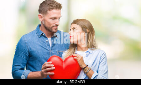 Coppia giovane in amore azienda cuore rosso su sfondo isolato con un fiducioso espressione sul viso intelligente pensare grave Foto Stock