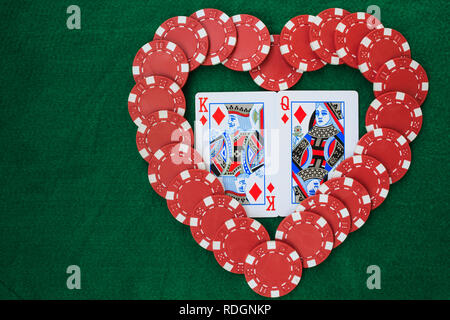 Cuore realizzato con chips, con il re e la regina dei diamanti, su uno sfondo verde tabella. Vista da sopra con copia spazio. Foto Stock