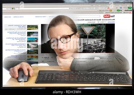 Giovane donna seduta a un computer per navigare in Internet, la visualizzazione di un video sul sito di YouTube, vista dall'interno del computer Foto Stock