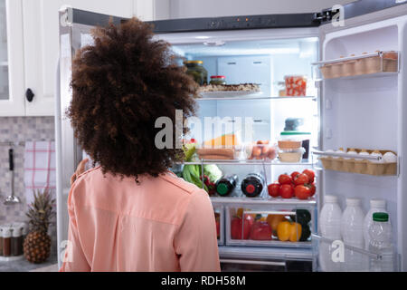 Vista posteriore di una donna confusa alla ricerca di cibo in un frigorifero aperto Foto Stock