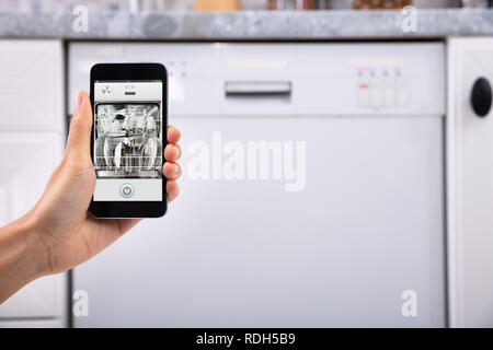 Close-up di una donna di mano lavastoviglie operativo con il telefono cellulare Foto Stock