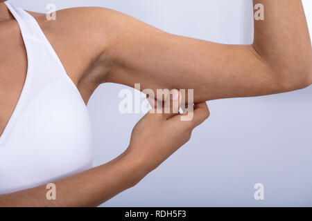 Close-up di montare una giovane donna controllando il grasso eccessivo sulle sue braccia su sfondo bianco Foto Stock