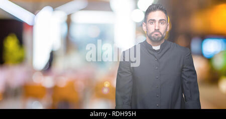 Giovane sacerdote cristiano su sfondo isolato premuto e la preoccupazione per la sofferenza, gridando arrabbiato e paura. Triste espressione. Foto Stock