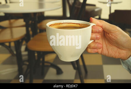 Mano d'uomo bianco di contenimento tazza di caffè caldo con sfocate stile Francese Cafe in background Foto Stock