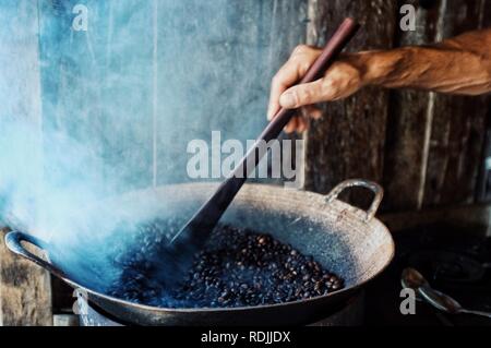 Paksong / Laos - Lug 06 2011: torrefazione di caffè in modo tradizionale in un wok, mentre lo sterzo in piccola scala di produttori biologici Foto Stock