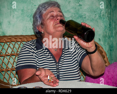 Un senior donna con una bottiglia di vino e un gran numero di pillole in mano di diversi colori e dimensioni Foto Stock