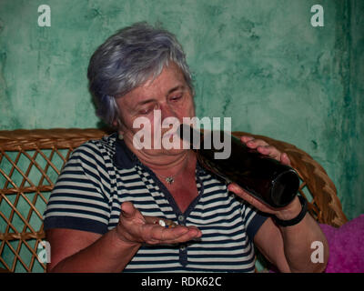 Un senior donna con una bottiglia di vino e un gran numero di pillole in mano di diversi colori e dimensioni Foto Stock