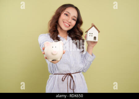 Edificio, ipoteca, investimenti immobiliari e concetto di proprietà - close up di donna holding home o casa del modello e di salvadanaio Foto Stock