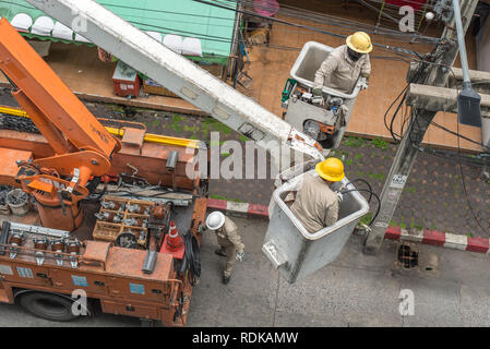 Bangkok, Tailandia - 22 Luglio 2018: elettricisti in uniforme riparare un polo elettrico essendo su piattaforma di lavoro aerea. Foto Stock