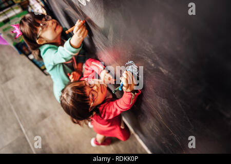 Vista dall'alto di due bambini soleggiata con gli occhiali disegno sulla lavagna Foto Stock