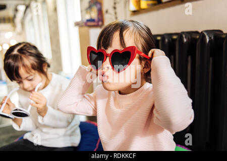 Carino divertente ragazza dai capelli scuri che indossa rosso brillante occhiali da sole Foto Stock