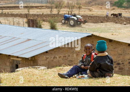 Due ragazzi ridere e godere della loro luch presso una scuola di villaggio nel distretto Butha-Buthe del Lesotho come un agricoltore lavora un campo in background. Foto Stock