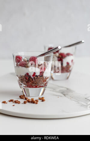 Due bicchieri di più livelli di cereali e yogurt con lamponi su un vassoio in marmo su sfondo bianco Foto Stock