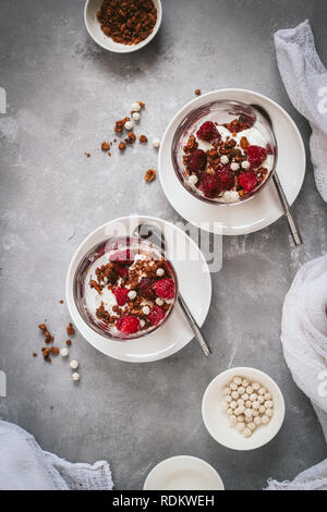 Lay piatto con vetri stratificati di cereali e yogurt con lamponi su sfondo scuro Foto Stock