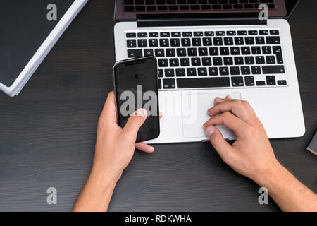 Mans mani digitando su smart phone mentre si lavora sul computer portatile su vintage tavolo in legno. Mani digitando su una tastiera. Vista superiore, business office workp Foto Stock