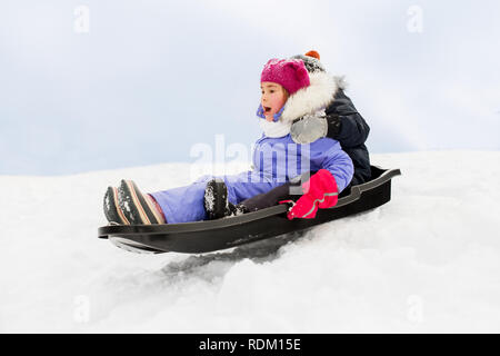 Bambini piccoli scorrevole sulla slitta giù per la collina in inverno Foto Stock