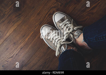 Converse All Star scarpe / formatori con un animale stampa, fotografati contro il pavimento in legno Foto Stock