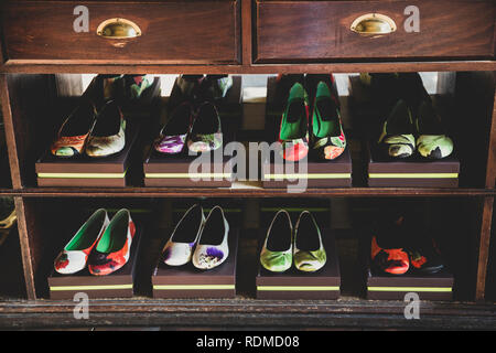 Angolo alto close up di scarpe con tacco con colorati motivi floreali su confezioni marroni allineate su scaffalature di legno. Foto Stock