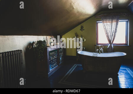 Vista interna del sottotetto bagno con pavimento in legno, verde pareti e soffitto in rame, rame autoportante slipper vasca da bagno e gabinetto vintage. Foto Stock