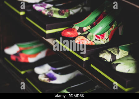 Angolo alto close up di scarpe con tacco con colorati motivi floreali su confezioni marroni allineate su scaffalature di legno. Foto Stock