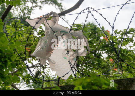 Una vista ravvicinata di un bianco busta di plastica che ha catturato nel filo spinato sulla sommità di una recinzione in cemento armato Foto Stock