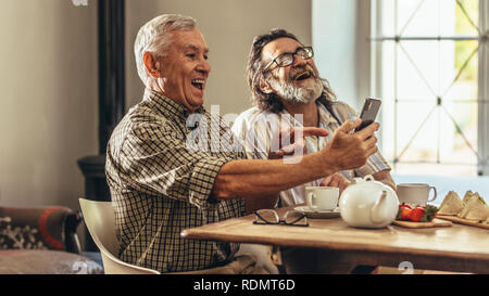 Alti uomini guardando le vecchie fotografie di loro nel telefono cellulare e ridere. Due uomini anziani guardando le vecchie fotografie insieme e ridere. Foto Stock