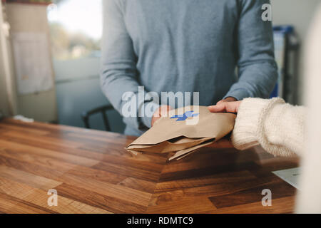 Ritagliato colpo di farmacia consegna farmaci per il cliente alla cassa. Il farmacista dando la medicina prescritta per il cliente in farmacia. Foto Stock