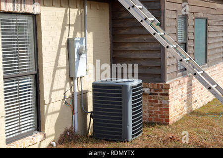 Grigio il condensatore del condizionatore aria unità di compressore accanto al dipinto di casa di mattoni con scaletta contro house Foto Stock