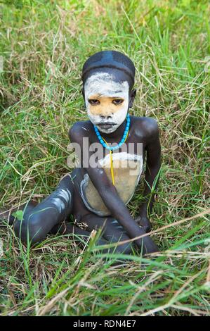 Surma ragazzo con trattamenti per il viso e per il corpo dipinto giacente su erba, Kibish, Omo River Valley, Etiopia, Africa Foto Stock