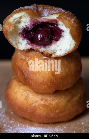 Donuti con ciliegie su sfondo nero. Ciambelle fresche. Foto Stock