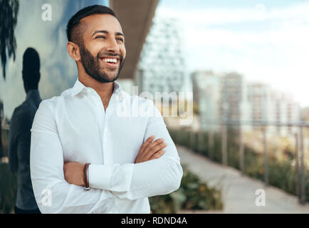 Ritratto di un giovane fiducioso sorridente uomo indiano con le braccia incrociate guardando in lontananza Foto Stock