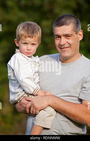 Padre che porta il suo giovane figlio nelle sue braccia Foto Stock