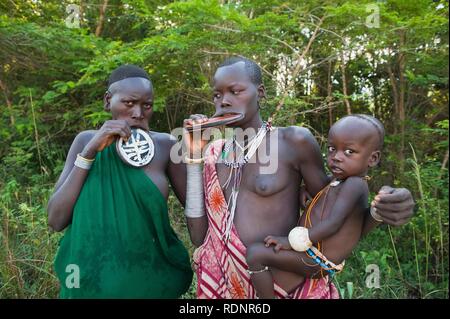 Due donne Surma con enorme labbro arrotondato piastre e tenendo un bambino, Kibish, valle dell'Omo Valley, Etiopia, Africa Foto Stock