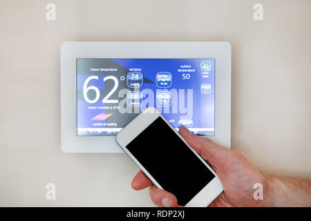 Maschio di mano azienda smart phone per azionare il riscaldamento o il raffreddamento del termostato per la casa Foto Stock