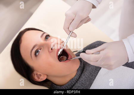 Close-up di donna di denti essendo controllato dal dentista con specchio dentale e Scaler Foto Stock