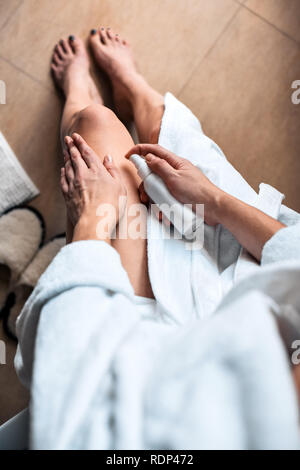 La ragazza in bagno mette crema anti-cellulite, siero sulle gambe e il corpo. Cura del corpo concetto. Vista superiore Foto Stock