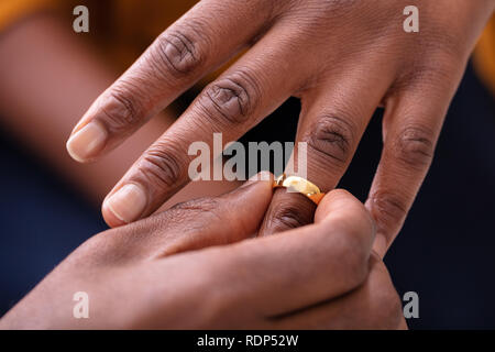 Close-up di mano d'uomo mettendo Golden anello di fidanzamento sulla donna del dito Foto Stock