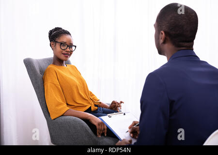 Giovane donna africana seduta vicino psicologo con appunti per trattare la depressione Foto Stock