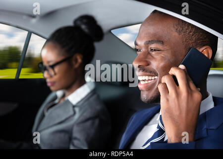 Happy Businessman seduto all'interno dell'auto accanto alla sua collega femmina parlando al cellulare Foto Stock