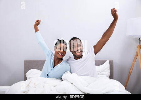 Ritratto di un felice giovane africano giovane alzando le braccia sul letto Foto Stock